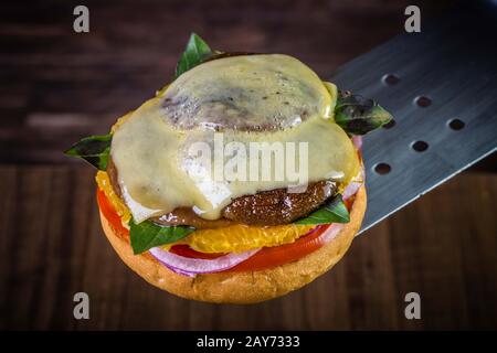 Hamburger végétarien avec fromage, orange, feuilles de basilic, champignons shiitake et oignon violet sur table en bois et fond rustique Banque D'Images