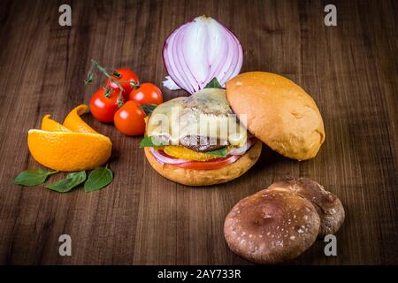 Hamburger végétarien avec fromage, orange, feuilles de basilic, champignons shiitake et oignon violet sur table en bois et fond rustique Banque D'Images