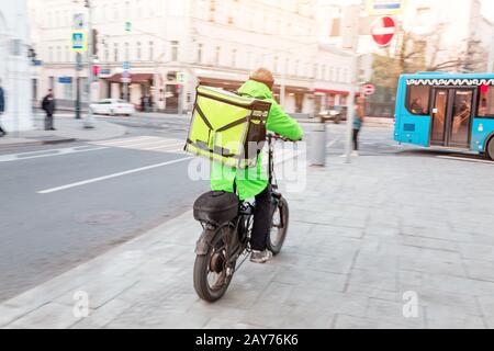 Homme de livraison avec sac à dos plein de délicieux vélo de conduite alimentaire sur le trottoir, effet flou de mouvement Banque D'Images