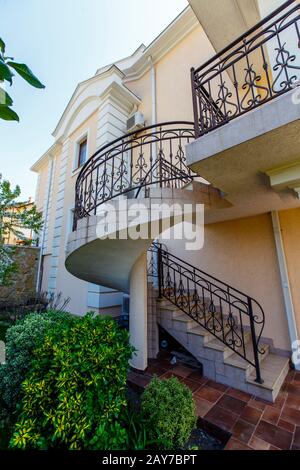 Un escalier en béton en spirale avec des rampes en fer forgé mène au deuxième étage du cottage. Cottage de style italien avec murs blancs, une cour W Banque D'Images