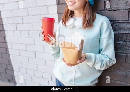 heureuse femme asiatique à la mode boire du café et manger des nouilles wok dans la rue de la ville. Concept de livraison de nourriture fastaway à emporter Banque D'Images