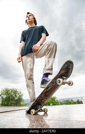 Un jeune patineur se tient avec un skateboard sur l'arrière-plan du paysage de la ville Banque D'Images