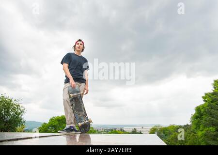 Un jeune patineur se tient avec un skateboard sur l'arrière-plan du paysage de la ville Banque D'Images