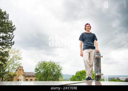 Un jeune patineur se tient avec un skateboard sur l'arrière-plan du paysage de la ville Banque D'Images