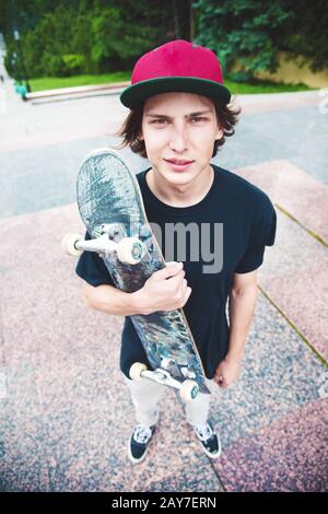 Un jeune patineur se tient avec un skateboard sur l'arrière-plan du paysage de la ville Banque D'Images