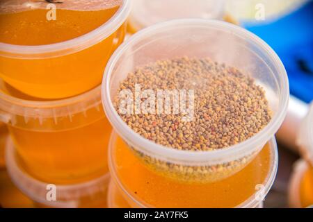 Granules de pollen d'abeilles dans un bocal en plastique se tenant sur des bocaux de miel Banque D'Images