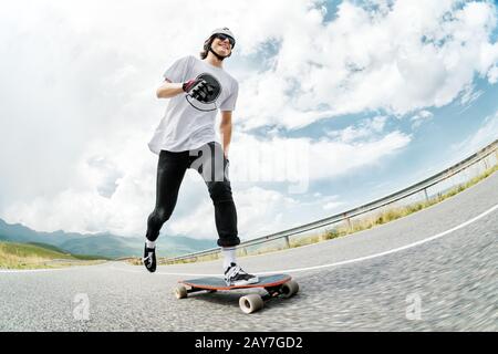 Un gars dans un casque et des lunettes de soleil accélère la poussée de son pied sur son long-board Banque D'Images