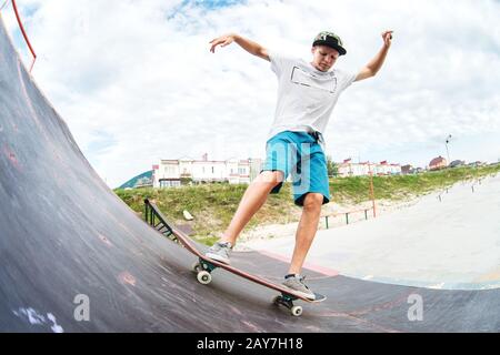 Un patineur pour adolescents monte sur une rampe sur un skateboard dans un parc de skate Banque D'Images