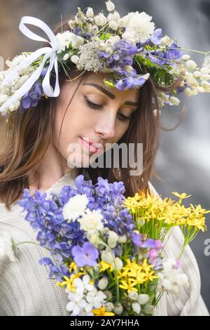 Portrait d'une fille avec une couronne sur sa tête et un bouquet de fleurs dans ses mains contre une chute d'eau Banque D'Images