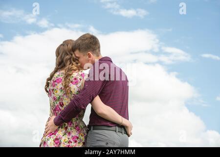 Vue de l'arrière. Jeune couple embrassant baisers contre le ciel bleu et les nuages blancs. Banque D'Images