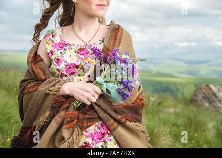 Une fille enveloppée dans un plat et dans une robe colorée contient un bouquet de fleurs sauvages Banque D'Images