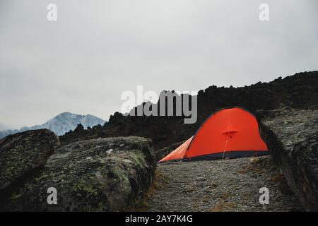 Une tente orange est haute dans les montagnes entre deux hautes roches Banque D'Images