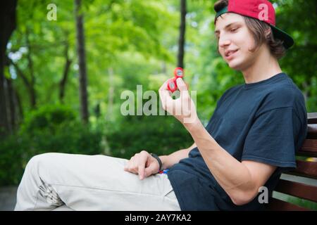 Un hipster à poil long dans une casquette est assis sur un banc et tourne un disque de fidget Banque D'Images