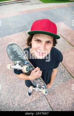 Un jeune patineur se tient avec un skateboard sur l'arrière-plan du paysage de la ville Banque D'Images