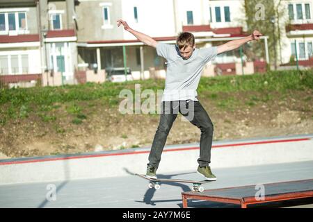 Un jeune gars glisse sur un skateboard dans un manuel sur un skatepark sur l'arrière-plan de la maison Banque D'Images