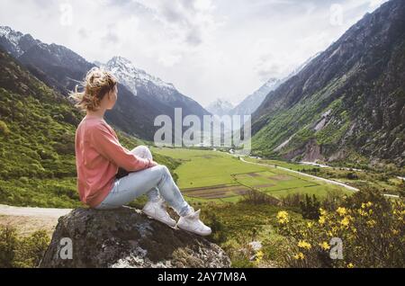 Une belle fille se trouve sur un rocher dans les montagnes et regarde le beau paysage d'une vallée de montagne Banque D'Images