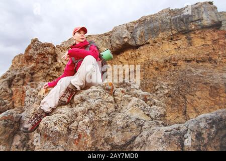 Un voyageur de fille est assis sur un rocher haut dans les montagnes du Caucase dans le contexte de coucher de soleil de rochers et de coucher de soleil Banque D'Images