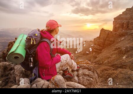 Un voyageur de fille est assis sur un rocher haut dans les montagnes du Caucase dans le contexte de coucher de soleil de rochers et de coucher de soleil Banque D'Images