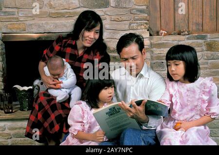 Texas: Père vietnamien lisant à ses enfants pendant que sa femme tient leur bébé dans leur maison d'Austin. ©Bob Daemmrich Banque D'Images