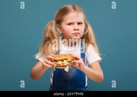 Adorable petite fille en chemise blanche et combinaison jean avec hamburger Banque D'Images