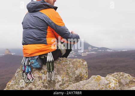 Hipster - un grimpeur dans une veste en duvet et un bonnet tricoté est assis et repose sur le sommet d'un rocher Banque D'Images