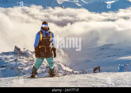 Un snowboarder professionnel avec un sac à dos se tient sur la neige haut dans les montagnes contre le fond de nuages bas et le Banque D'Images