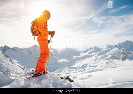 Un skieur dans un ensemble orange avec un sac à dos sur son dos portant un casque et avec des bâtons de ski dans ses mains est debout sur un preci Banque D'Images