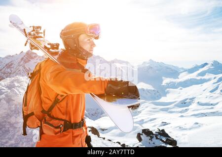 Portrait d'un Skieur dans un ensemble orange avec un sac à dos sur son dos et des skis sur ses épaules dans un casque se tient sur un agai de roche Banque D'Images