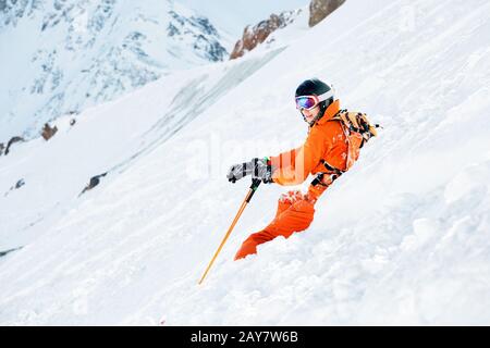 Un skieur dans un ensemble orange et avec un sac à dos est assis heureux dans la neige après la chute. Banque D'Images