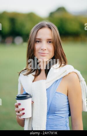 Photo d'une jeune femme caucasienne attrayante avec des cheveux sombres, boissons café, vêtu d'une tenue décontractée, regarde directement l'appareil photo, se tient à l'extérieur, aime RE Banque D'Images