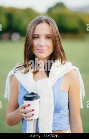 Une belle jeune femme européenne aux cheveux droits, vêtue d'une tenue décontractée, boit du café à emporter, se promener en plein air, se déchire Banque D'Images