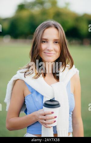 Portrait extérieur d'une jolie femme européenne avec look apaisant, vêtu de vêtements décontractés, conserve le café à emporter, aime le temps libre, respire Banque D'Images