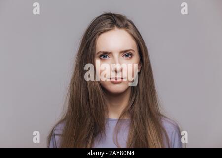 Portrait d'une femme brunette sérieuse avec une peau saine, regarde en toute confiance l'appareil photo, a des cheveux droits foncés, isolés sur fond gris studio. Prét Banque D'Images