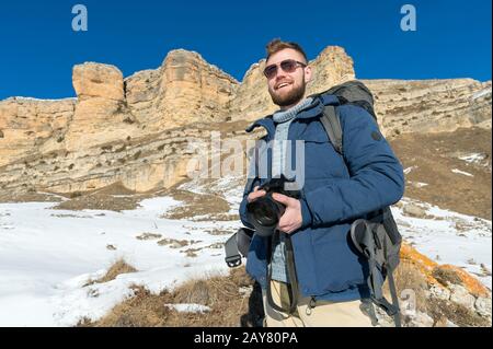 Portrait UN photographe hipster barbu avec un sac à dos et porter des lunettes de soleil avec un grand sac à dos sur ses épaules se tient esprit Banque D'Images