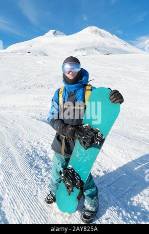 Un snowboarder professionnel se tient avec son snowboard contre le ciel bleu Banque D'Images