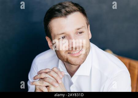 Photo intérieure d'un homme rasé et charmant, porte une élégante chemise blanche, centrée sur la distance, en étant profondément pensées. Posture de l'homme Banque D'Images