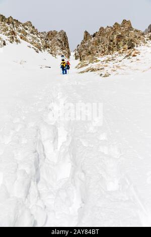 Les skieurs extrêmes grimpent au sommet le long du coulier entre les rochers avant la descente du freeride backcountry Banque D'Images