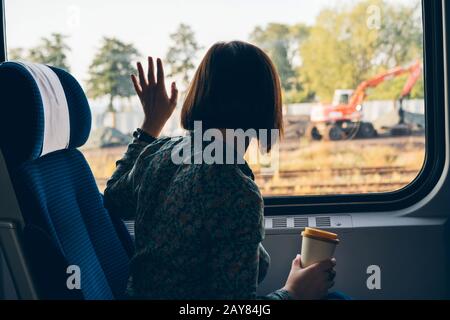 Une femme assise près de la fenêtre d'un train de banlieue avec une tasse à café en bambou Banque D'Images