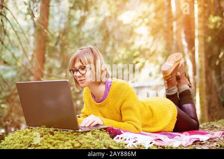 Image tonifiée d'un portrait d'une fille indépendante dans un pull jaune et des lunettes regardant de manière réfléchie l'écran de l'ordinateur portable dans le natur Banque D'Images