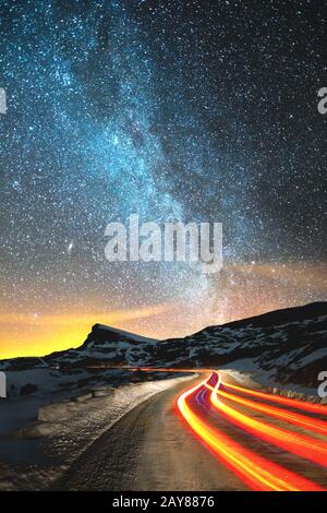 Paysage de nuit. Ciel nocturne avec une voie lactée de l'hémisphère nord et des étoiles. La route de nuit éclairée par la voiture serpe Banque D'Images