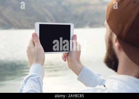 Hipster personne tenant dans les mains tablette numérique avec écran vide, homme photographie sur ordinateur sur fond nature extérieur Banque D'Images