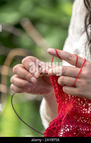 Mains d'une femme qui crochets avec la laine rouge / knits en face d'arrière-plan flou Banque D'Images