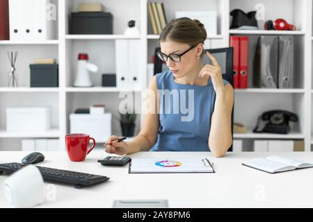 Une jeune fille est assise au bureau, tenant un stylo dans sa main et compte sur la calculatrice. Avant la fille lie Banque D'Images