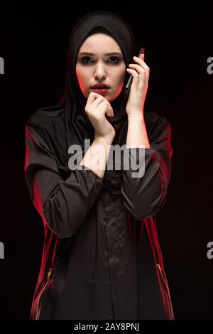 Portrait de peur peur grave belle jeune femme musulmane portant le hijab noir appelant à l'aide sur fond noir Banque D'Images