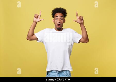 Jeune homme africain américain étonné vêtu d'un maillot blanc décontracté qui a excité le regard fasciné, pointant l'index doigt à la cdp Banque D'Images