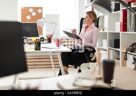 Une jeune fille est assise sur une chaise dans le bureau et contient des documents et d'un crayon dans ses mains. Banque D'Images