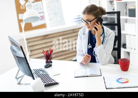 Une jeune fille dans un peignoir blanc est assise au bureau, parler au téléphone et tenir un stylo dans sa main. Un stethos Banque D'Images