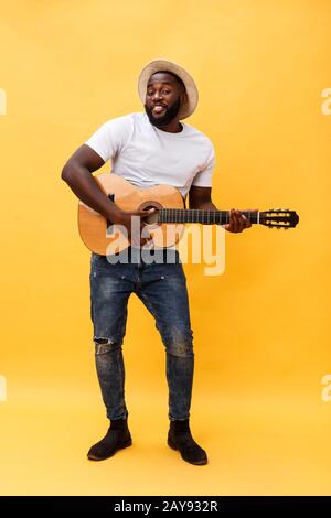 Photo de pleine longueur artistique excité homme jouant de sa guitare en suite. Isolé sur fond jaune. Banque D'Images