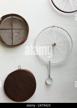 Tamis, roues de bicyclettes et une louche accrochées sur un mur blanc d'une maison traditionnelle de Lefka Chypre Banque D'Images