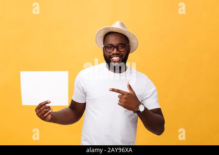 Photo de young smiling african-american man holding blank blanc et en pointant sur elle, sur fond jaune, copy space Banque D'Images